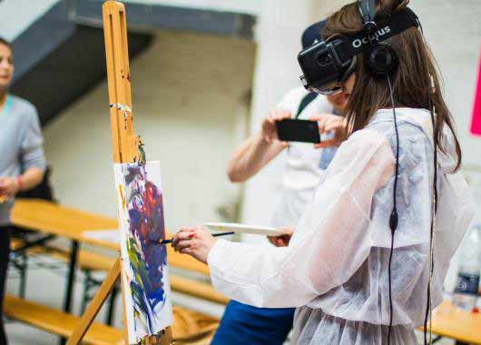 Une jeune femme peint une toile équipée d'un casque de réalité virtuelle sur les yeux.
