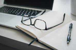 Un ordinateur portable, une paire de lunettes, un cahier ouvert et un stylo.